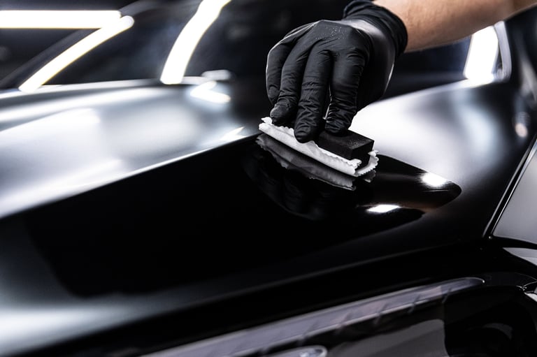 Detailing studio employee applying ceramic coating to black car paint