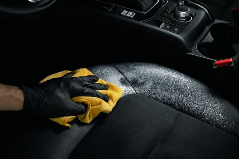 car interior cleaning and detailing service. man cleaning black alcantara leather seat with foam detergent and microfiber cloth