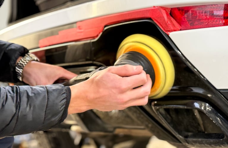 A car service worker polishes the car body with a polishing machine. Detailing and polishing of the car.