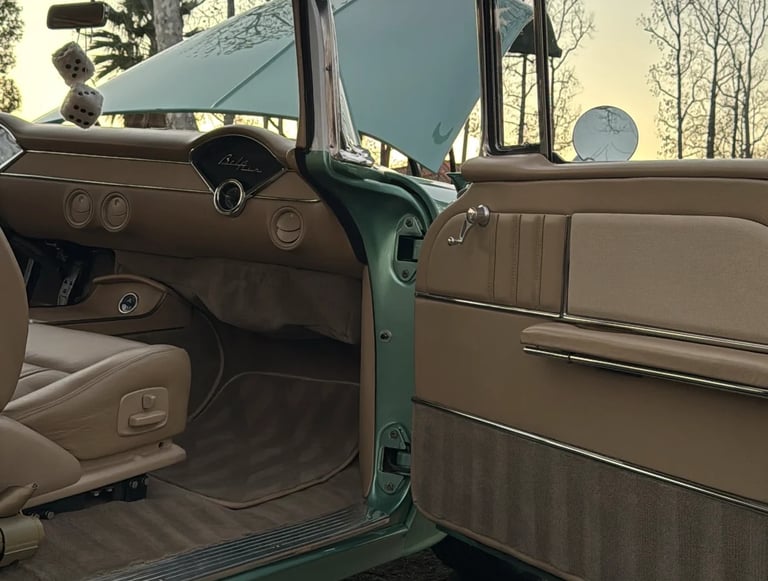 Open driver-side door of a vintage green and tan truck showing tan interior, steering wheel, and dashboard