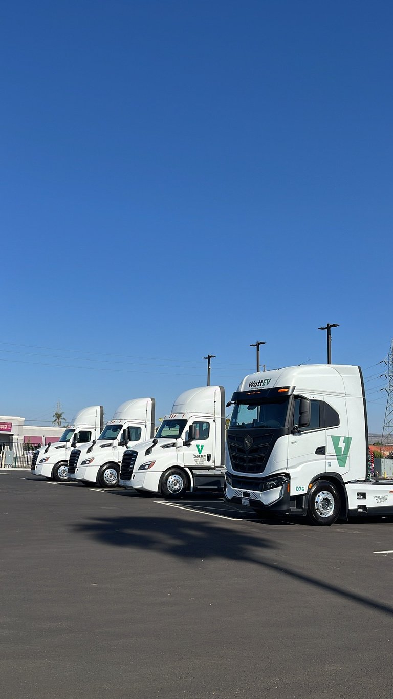 Row of white commercial trucks parked in a line at a facility under a clear blue sky